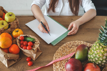 Doctor nutritionist writing case history in the office. Young woman dietitian prescribing recipe