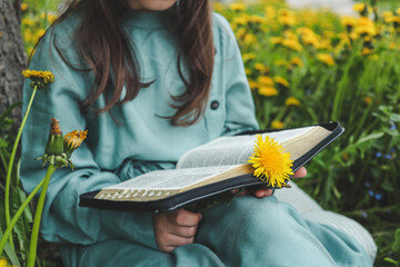 Little girl reading bible in dandelion field, christian concept