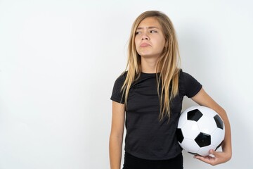 Dissatisfied beautiful caucasian teen girl wearing sportswear  over white wall purses lips and has unhappy expression looks away stands offended. Depressed frustrated model.