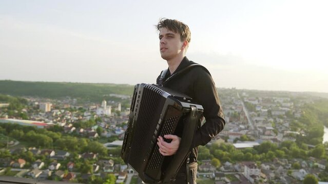 A man plays the accordion at sunset with a view of the city. Smooth moving