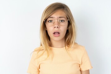 Obraz premium Emotional attractive beautiful caucasian teen girl wearing orange T-shirt with opened mouth expresses great surprise and fright, stares at camera. Unexpected shocking news and human reaction.