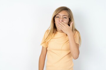 Sleepy beautiful caucasian teen girl wearing orange T-shirt over white wall yawning with messy hair, feeling tired after sleepless night, yawning, covering mouth with palm.