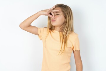 Fototapeta premium Displeased beautiful caucasian teen girl wearing orange T-shirt over white wall plugs nose as smells something stink and unpleasant, feels aversion, hates disgusting scent.