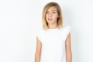 Portrait of dissatisfied beautiful caucasian teen girl wearing white T-shirt over white wall smirks...