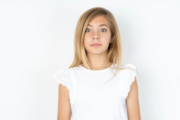 Stunned beautiful caucasian teen girl wearing white T-shirt over white wall stares reacts on shocking news. Astonished kid holds breath - obrazy, fototapety, plakaty