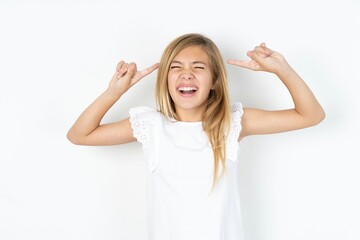 Fototapeta premium Photo of crazy beautiful caucasian teen girl wearing white T-shirt over white wall screaming and pointing with fingers at hair closed eyes