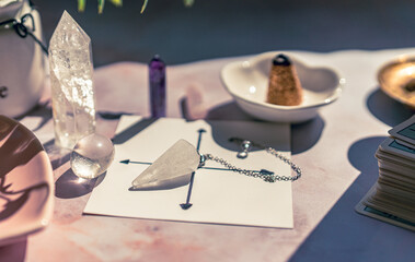 Gemstones for esoteric spiritual practice. Rock crystal pendulum on the table. Divination with a pendulum. - obrazy, fototapety, plakaty