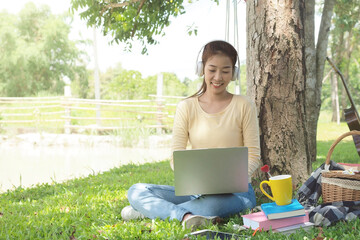 Asian student girl is studying  by laptop in nature with tree. Asian student is happy in study online and drinking coffee. Education in online life concept. Study Online in vacation.