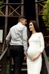 a man with a pregnant woman are sitting on a wooden staircase near the entrance to the house. beautiful pregnant couple