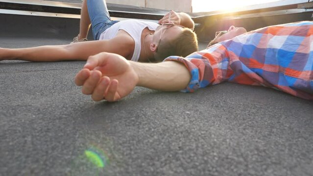 Two young gays lying on roof and smoking with bright sunlight at background. Men resting and enjoying life together. Friends relaxing outdoor at sunset time. Beautiful bottom view Slow mo Close up