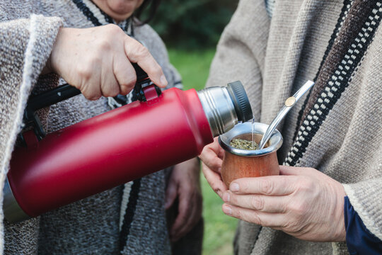 Cropped people in woolen ponchos sharing hot tea in park