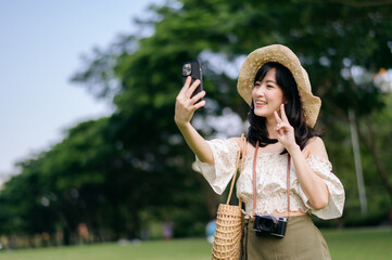 Portrait of asian young woman traveler with weaving hat, basket, mobile phone and camera on green public park background. Journey trip lifestyle, world travel explorer or Asia summer tourism concept.