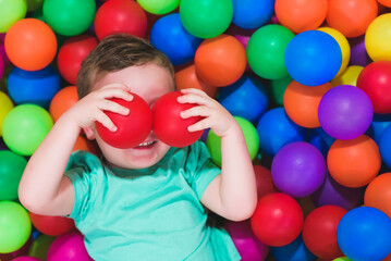 Fototapeta na wymiar Portrait of funny little boy playing in ball pit and enjoying time in children's play and entertainment area, copy space