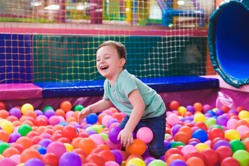 Happy laughing child laughing in an indoor play center. Children playing with colored balls in the playground ball pool. Party