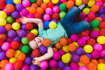 Fototapeta na wymiar Smiling boy playing lying on colorful balls in the park