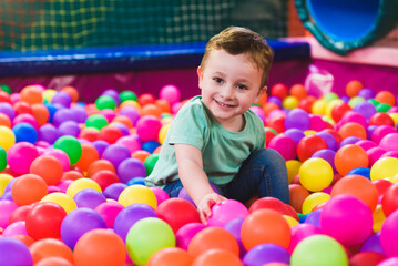 Fototapeta na wymiar Happy laughing child laughing in an indoor play center. Children playing with colored balls in the playground ball pool. Party
