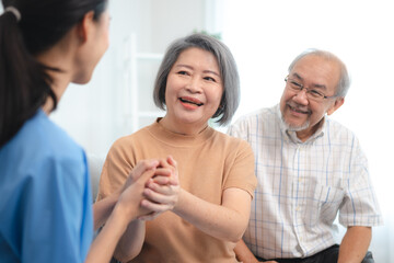 Smiling young nurse in uniform sitting with senior male and female couple at home assuring and building them in confidence about recovery in health