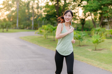 Fit Asian young woman jogging in park smiling happy running and enjoying a healthy outdoor lifestyle. Female jogger. Fitness runner girl in public park. healthy lifestyle and wellness being concept