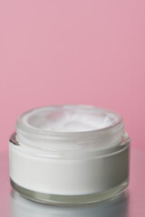 Glass jar with white face cream moisturiser on pink background.