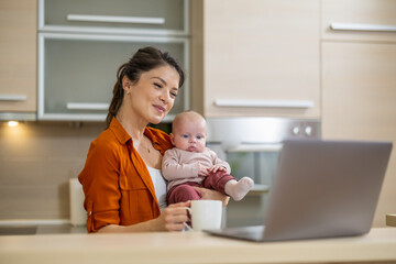 Obraz na płótnie Canvas Mother with baby using laptop in kitchen