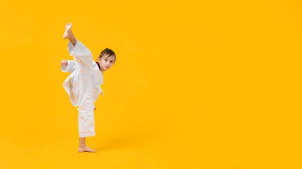 Fotobehang Banner: Asian-Australian girl poses in martial arts Practice taekwondo, karate, judo against a yellow background in the studio. Asian kids karate or Taekwondo martial arts. Sport kid training action. © VR Studio