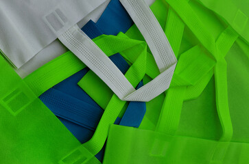 green, white and blue polypropylene bags. pile of tote bags of non-woven fabrics