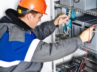 Electrician in helmet or instrumentation fitter checks capacity of batteries of automatic control system of gas distribution station with multimeter.