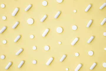 Various white medication tablets and capsules on yellow background. Concept of healthcare and medicine. Top view, pattern