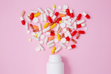 White bottle container with various colorful medication tablets and capsules on pink background. Concept of healthcare and medicine. Top view