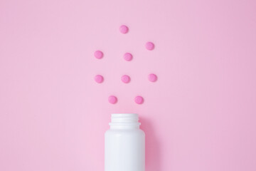 White bottle container with medication tablets on pink background. Concept of healthcare and medicine. Top view
