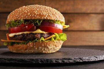 fresh burger burger of bun, onion, tomato, ketchup, mayonnaise, cheese, lettuce, meat patty, beef, on a black table and black plate on a rustic wooden background