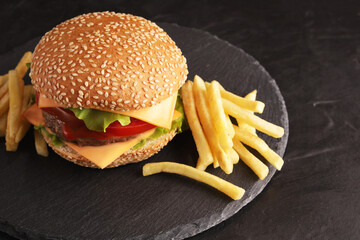 fresh burger burger made of bun, onion, tomato, ketchup, mayonnaise, cheese, lettuce, meat patty, beef, fries and ketchup sauce and a glass of Coke on a black table and black plate on a rustic wooden 