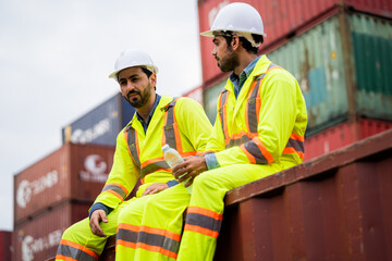 Two worker engineer sitting near a shipping container looks exhausted after working in the work area for a long time. He looks tired and sleepy or unemployed.