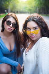 Two young latin female friends walking at the woods. Embrace each other and laughing. Friends making selfie. Two beautiful latin young women making selfie