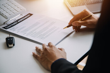 A car rental company employee is handing out the car keys to the renter after discussing the rental details and conditions together with the renter signing a car rental agreement. Concept car rental.