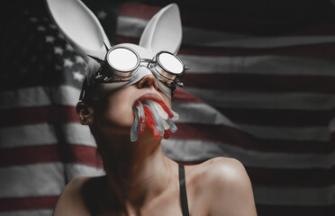 woman in a white rabbit mask and biker glasses on the background of the American flag with jelly...