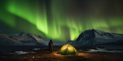 A man camping in wild northern mountains with an illuminated tent viewing a spectacular green northern lights aurora display.