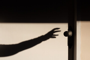A sombra de um braço com mão a querer abrir uma porta branca fechada.