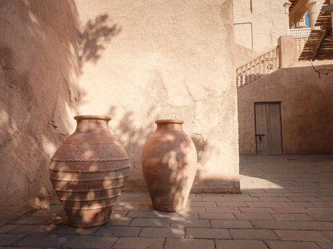 decorative weathered earthenware vases standing outdoors in the sunshine in a courtyard or park in Al seef old historical district with traditional Arabic architecture.