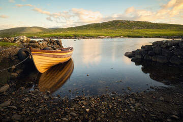 Obraz premium Beautiful morning landscape scenery with old wooden fishing boat reflected in lake with mountains in the background at Screebe, connemara national Park in County Galway, Ireland 