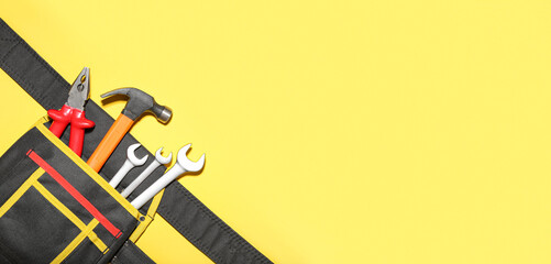 Tool belt with hammer, pliers and wrenches on yellow background with space for text