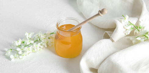 Jar of tasty acacia honey on light background