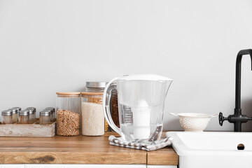 Fototapeta na wymiar Water filter jug with napkin on kitchen counter near light wall