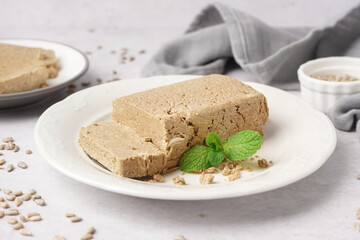 Plate with tasty halva and sunflower seeds on white table