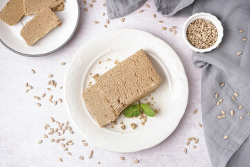 Plate with tasty halva and sunflower seeds on white background