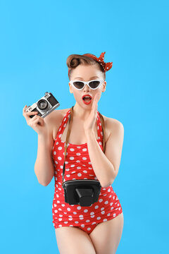 Shocked young pin-up woman in swimsuit with photo camera on blue background