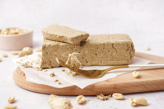 Board with tasty halva and peanuts on white background