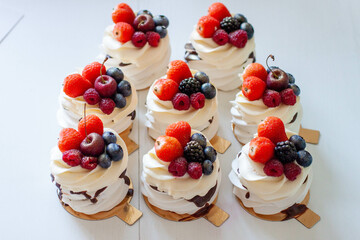 Delicious mini Pavlova meringue cakes decorated with fresh raspberry, strawberry and blueberry on white background