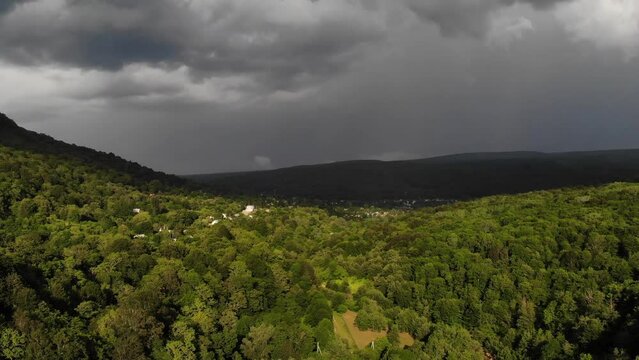 Aerial view of green trees, a picturesque almost invisible village in a stormy sky, overlooking the vast plains and distant mountains