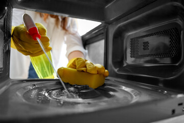 Housewife cleaning microwave oven with sponge in kitchen, view from inside - obrazy, fototapety, plakaty